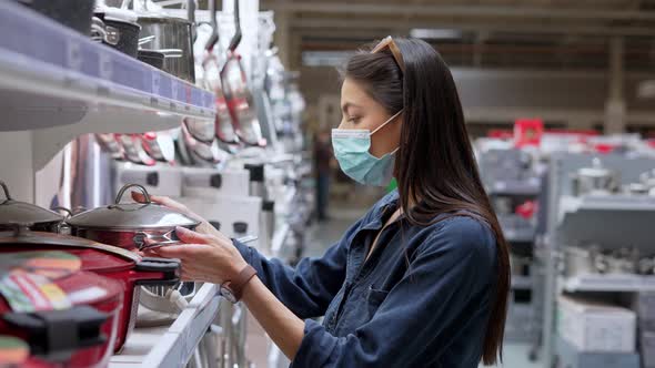 Young Woman in Face Protective Mask Choosing Metal Deep Pan for Cooking