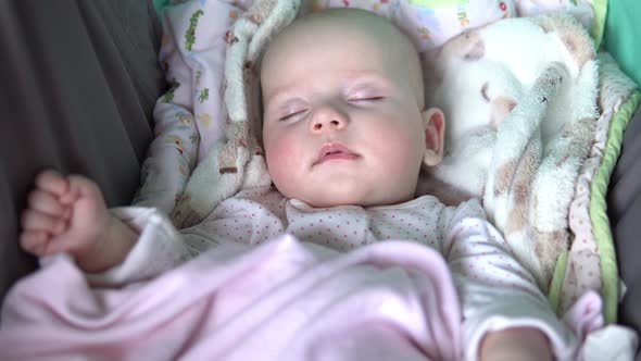 A Baby Is Sleeping with a Pacifier in Its Mouth in a Stroller. Face Close Up.