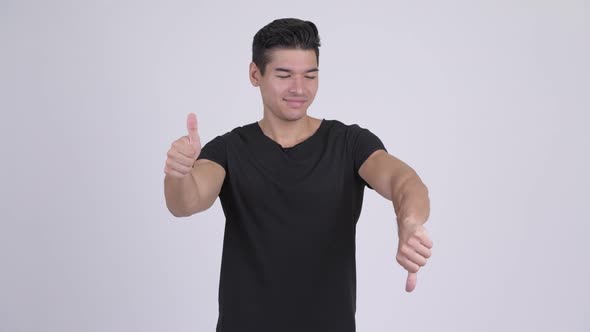 Young Handsome Multi-ethnic Man Choosing Between Thumbs Up and Thumbs Down