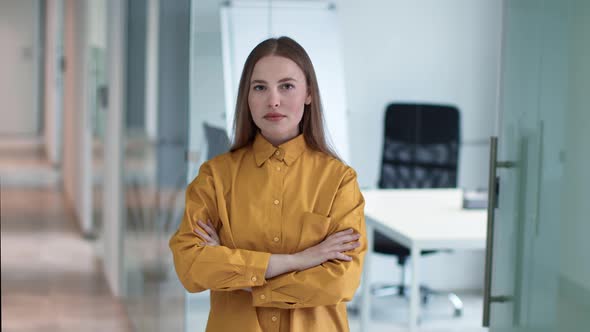 Indoors Portrait of Young Confident Woman Office Manager Posing with Folded Arms at Corporate