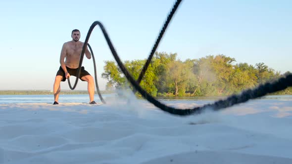 Sports Man Conducts Training with the Ropes on the Sandy Shore