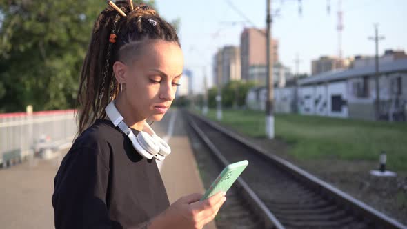 Happy Woman Writes a Message on a Smartphone on the Background of the Railway