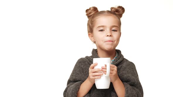 Small Charming Caucasian Kid Girl with Hair Buns and Cozy Woollen Sweater Drinking From Cup and