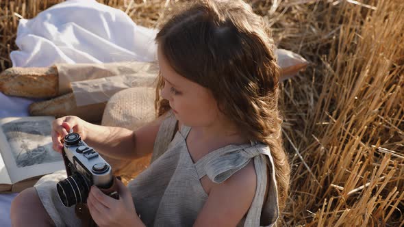 Serious Child Girl with Long Hair Sits on a Mown Wheat Field