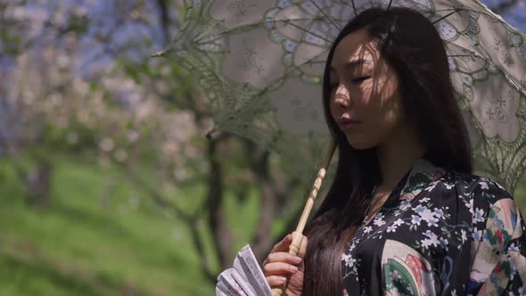 Young Asian Beautiful Woman Standing with White Sun Umbrella on Sunny Spring Day in Park Thinking