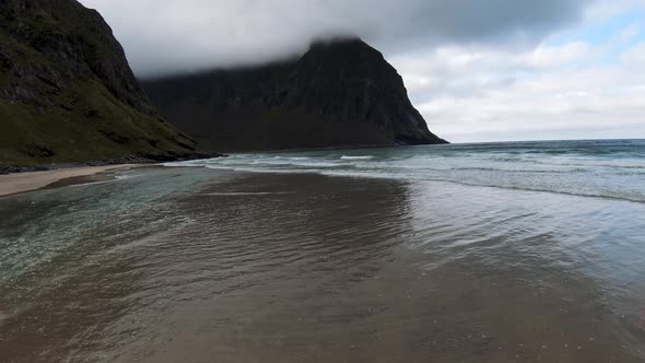 Flying over the ocean and the waves breaking at a beach (Kvalvika beach, Norway) overlooking the mou