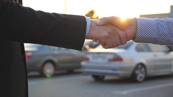 Two Businessmen Shaking Hands of Each Other with Cars in Parking at Background