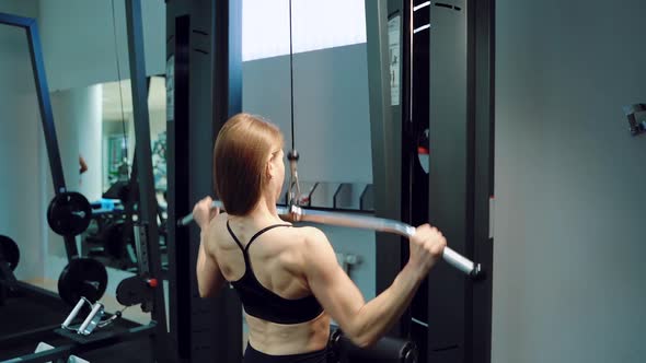 A strong woman in black top is doing vertical traction in the training in the fitness club.