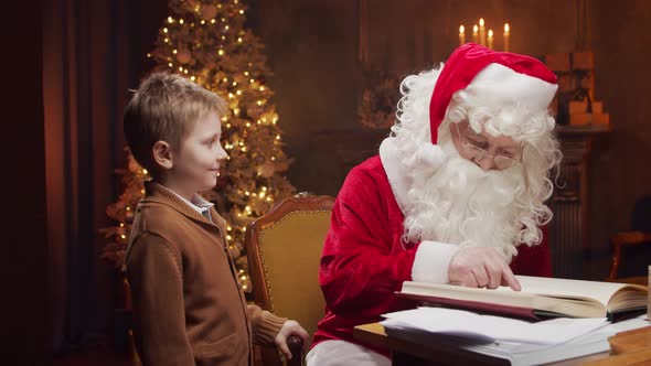 Santa Claus and little boy. Cheerful Santa is working at the table. Christmas concept.