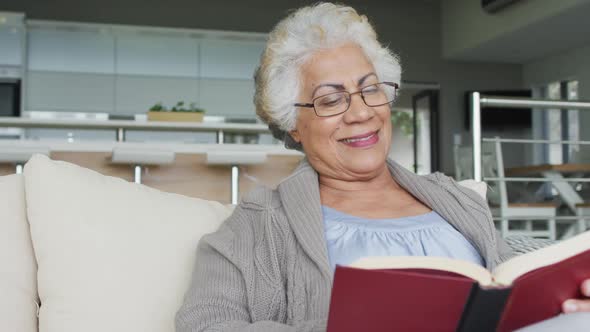 African american senior woman reading a book while sitting on the couch at home