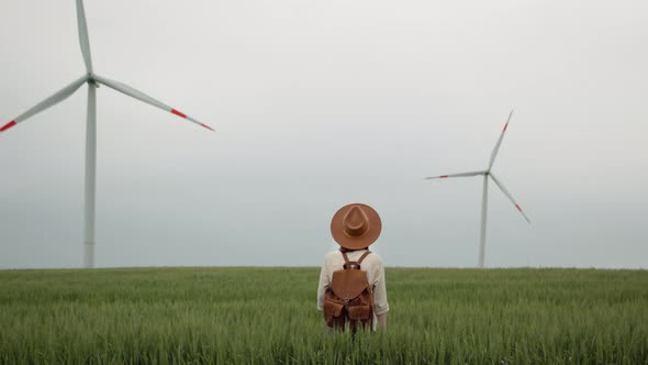 Portrait of a young girl with a backpack looking at the wind turbines in the field