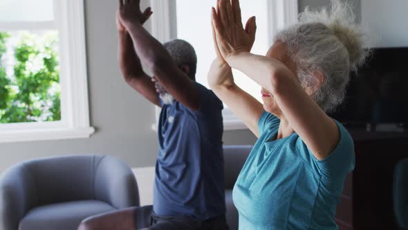 Mixed race senior couple practicing yoga together in the living room at home