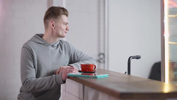 Side View of Positive Confident Millennial Student Sitting at Cafe Counter with Coffee Cup and