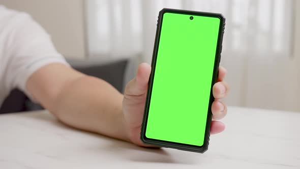 Man's hand shows mobile smartphone with green screen in vertical position isolated on green backgrou