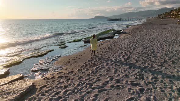 A girl in a yellow coat walks on the beach 4 K Aerial View