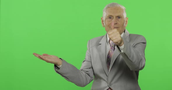 Elderly Businessman Points at Something and Thumb Up. Old Man in Formal Wear