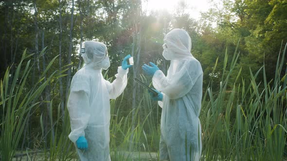 Chemists Wearing Ppe Suits Taking Sample of Water for Toxicity Testing Typing in Gadget Tablet