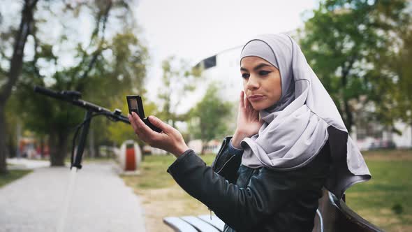 Portrait of Young Muslim Woman Looking at Herself Using Hand Mirror Outdoors in Park