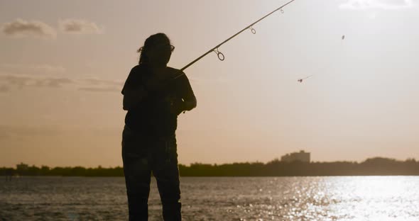 4K Silhouette of Latinx woman casting fishing rod against beautiful sunset