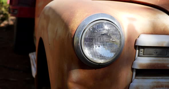 Slide left along the front of an old rusty vintage truck fender with glass headlight and grill in th