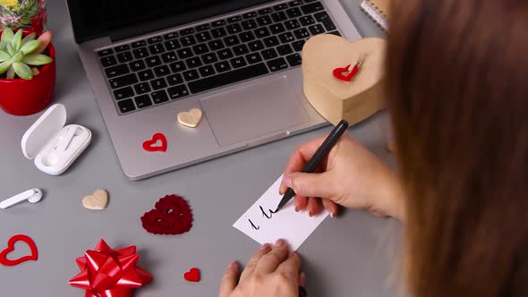 Young woman writing a card I LOVE YOU and wrapping valentine's day gift 