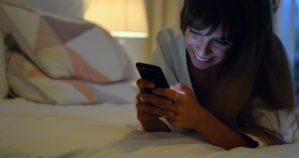 Woman using mobile on bed in bedroom at home