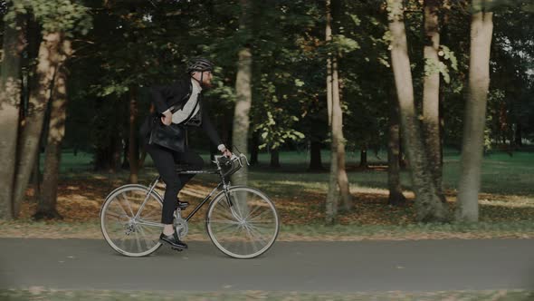 Businessman Riding a Bike in City Park Wearing Helmet and a Bag Side View