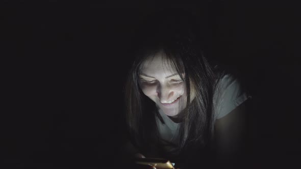 Young Woman in the Dark at Night Sits with a Phone in Social Networks