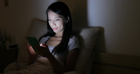 Woman use of mobile phone on bed at night 