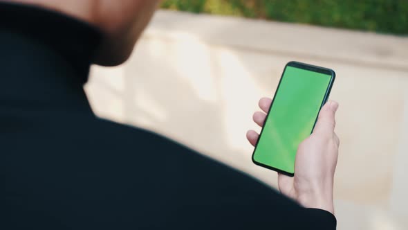 Over the Shoulder Shot of Man Using a Phone with a Green Screen Outdoors. Handsome Man Scrolling