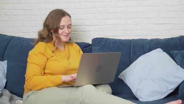 Woman is Sitting on the Sofa with Laptop and Typing Something