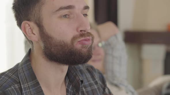 Portrait of Confident Man Eating Snacks and Drinking Beer with Friends at Home. Bearded Man Enjoying