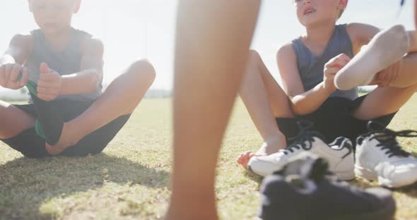 Video of happy diverse boys sitting on lawn and taking off socks alt