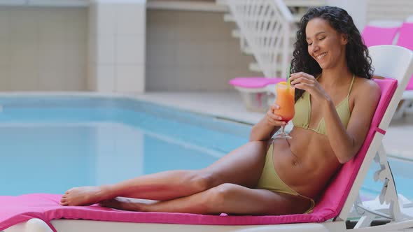 Happy Sexy Slender Tanned Hispanic Young Woman with Curly Long Hair Sunbathing By Pool in Spa Hotel