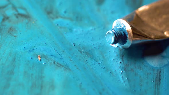 Blue color comes out of the tube. Open colored tube on floor. Paint brush paint on a blue surface