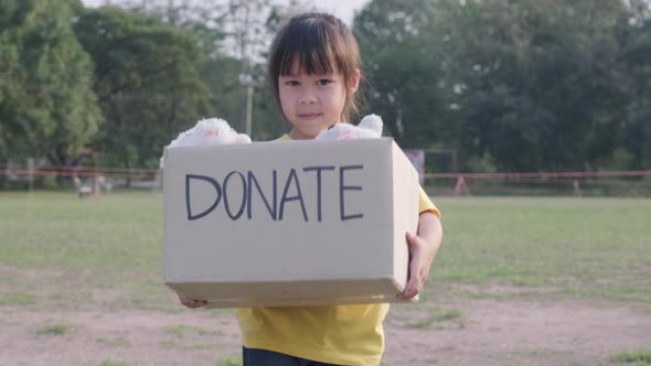 Cute little girl holding donation box with old dolls outdoors. Donation concept.