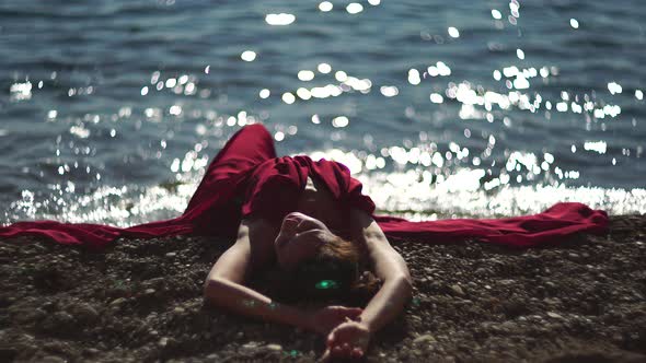 Side View a Young Beautiful Sensual Woman in a Red Long Dress Posing on a Beach with Calm Sea Bokeh