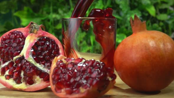 Pomegranate Juice Wave Is Falling Into a Glass on the Background of Greenery
