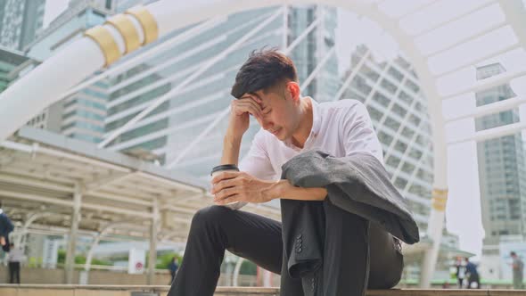 Asian business man sit outdoor feeling sad, stress and worry after unemployment from his company.