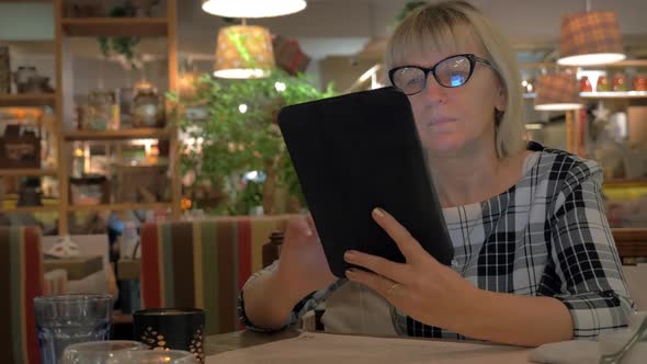 Senior Woman Browsing on Touch Pad in Cafe