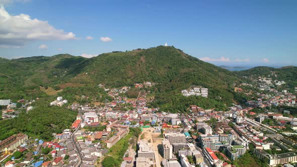 Buildings of Karon beach town with the big buddha on the top of the hill in tropical Phuket Thailand