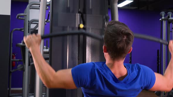 A Fit Man Trains on a Cable Tower in a Gym - Closeup From Behind