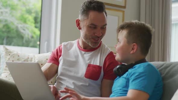 Happy caucasian father with son sitting in living room and using laptop