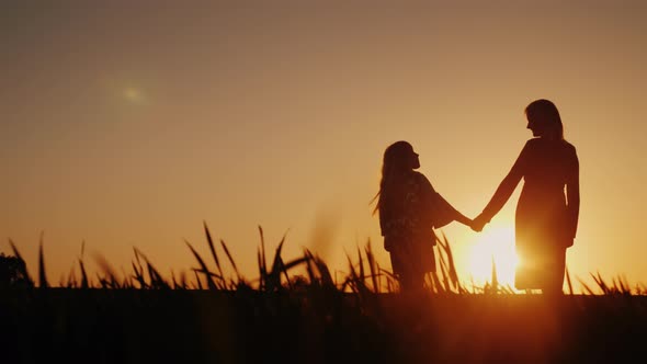 Mom and Daughter Are Admiring the Sunset, Holding Hands. Happy Childhood Concept