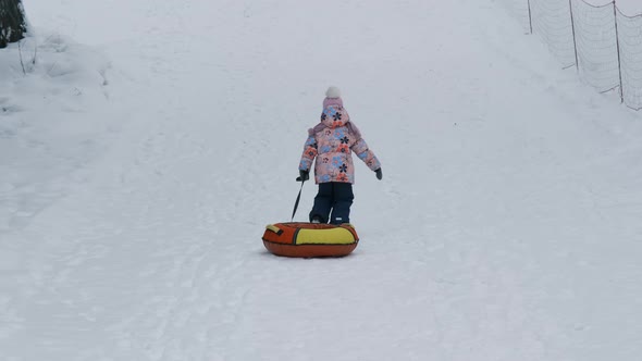 Little Girl Climbing a Hill with Snow Tube