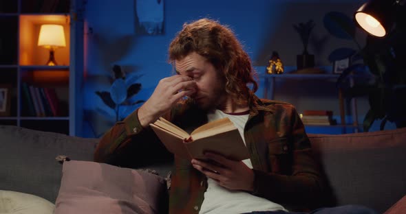Front View of Good Looking Guy Turning Page While Reading Late at Night and Looking Tired