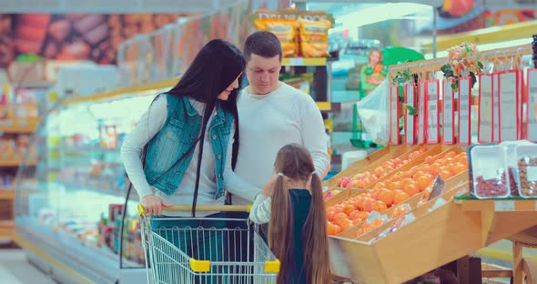 Mother Father and Daughter Approaching the Orange Shelf Choosing Some Oranges and Putting Them Into