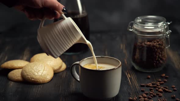 Slow Motion of Cream Being Poured Into a Cup of Coffee on Black Wood Table with Coffee Beans and