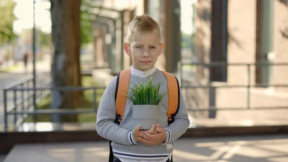 Portrait of the Male Pupil Standing Near School Carying Backpack Wearing Glasses Holding the Plant