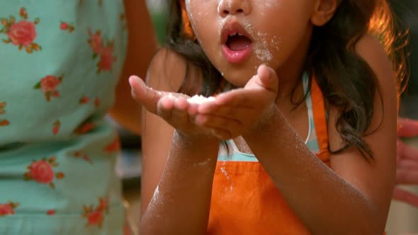 Girl blowing flour with her mother in kitchen